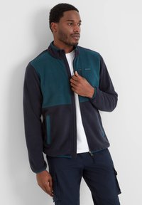 Fleece jacket in navy and teal, featuring a full zip, stand collar, and side pockets with contrasting accents and a smooth texture.