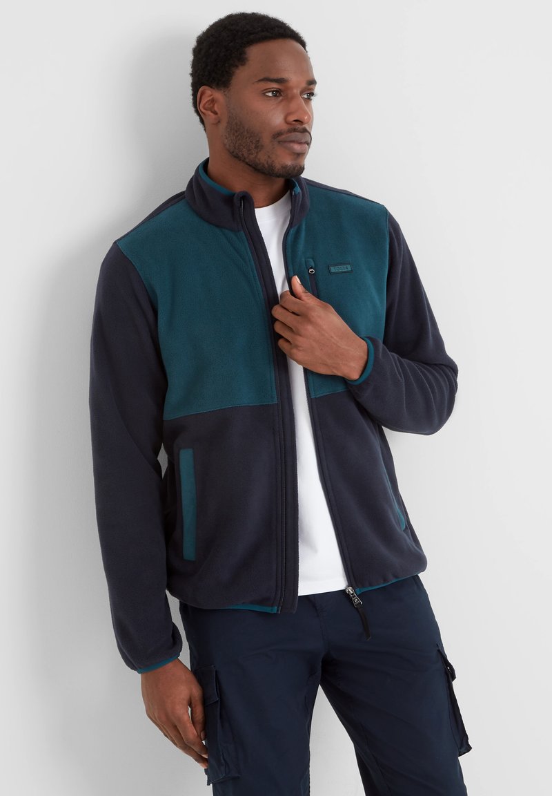 Fleece jacket in navy and teal, featuring a full zip, stand collar, and side pockets with contrasting accents and a smooth texture.