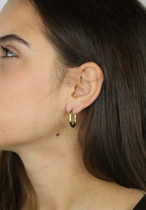 Złota kolczyk kołowy z polerowanym wykończeniem, o okrągłym kształcie, zabezpieczony zawiasem, prezentowany na uchu modelki na neutralnym tle.