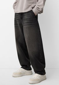 Musta denim-housut rennolla istuvuudella, joissa on sivutaskut ja hienovarainen kuluminen. Yhdistettynä beigeihin tennareihin, jotka esittelevät sileää rakennetta.