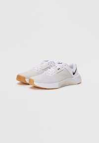 Pair of white and beige Nike training shoes with gum soles and black swoosh logo on the side against a white background.