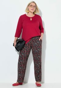 Červený top s dlouhým rukávem a detailem v podobě klíčové dírky; černé vzorované kalhoty s širokými nohavicemi; červené baleríny; černá psaníčko; velké náušnice; světlé pozadí.