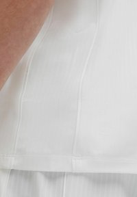 Ropa deportiva blanca con un tejido texturizado y un sutil patrón de rayas. El diseño incluye líneas limpias y un corte holgado.