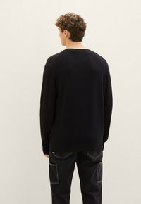Maglione nero lavorato a maglia con un motivo testurizzato, collo rotondo e spalle scese, abbinato a pantaloni cargo scuri con grandi tasche laterali.