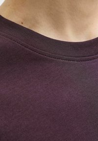 Ljubičasti pamučni T-shirt s ovratnikom s rebrastom teksturom. Prikaz izbliza fokusira se na izrez i detalje šivanja, naglašavajući glatku tkaninu.