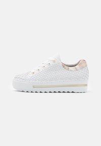White sneaker with woven material, gold-tone eyelets, textured back, and a white ribbed sole featuring a gold accent stripe.