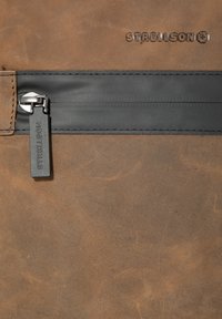 Borsa in pelle marrone con una cerniera nera e un'etichetta di estrazione rettangolare. Logo Strellson in rilievo sopra la cerniera, con una superficie texture.
