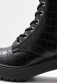 Zwarte veterlaarsjes met krokodillenpatroon van lakleer, zilverkleurige veterogen, gevoerde kraag en grove rubberen zool.