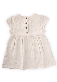 Robe en coton blanc avec des manches courtes à volants, tissu texturé et cinq boutons en bois dans le dos. Caractéristiques d'une jupe froncée.