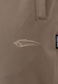 Braune Sporthosen aus dehnbarem Material mit glatter Textur, ausgestattet mit einem erhabenen Logo und einem Seitenschild zur Markenkennzeichnung.