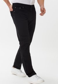 Black slim-fit jeans with a smooth texture, five-pocket design, metal hardware, and subtle stitching, paired with white sneakers.