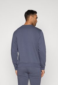 Πίσω όψη ενός ναυτικού μπλε φούτερ, φτιαγμένο από μαλακό ύφασμα, με στρογγυλή λαιμόκοψη και ριμπ μανίκια και τελειώματα. Συνδυασμένο με αντίστοιχες φόρμες.