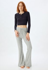 Mørkegrå langærmet cropped top med knapdetalje, parret med lysegrå ribbede flagrende bukser med elastisk talje.