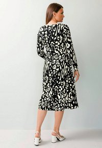 Schwarz-weißer Mittellanges Kleid mit einem Leopardenmuster, langen Ärmeln und einer taillierten Taille, die am Saum ausgestellt ist.