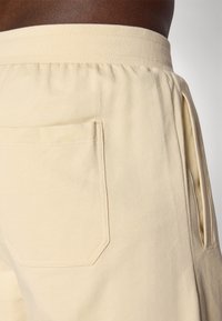 Ljusbeige shorts i mjukt tyg, med resårmidja och sidofickor. Bakfickan har en diskret sydd kontur.