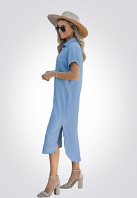 Vestido de camisa de denim azul claro con mangas cortas, aberturas laterales y un corte casual. Combinado con sandalias de tacón grueso y un sombrero de paja.