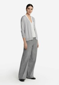 Ljust grå cardigan med knappar, kombinerad med vit t-shirt med v-ringning och lösa grå randiga byxor. Svarta skor fulländar outfiten.