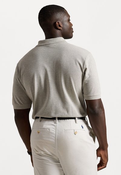 Camisa polo cinza com um malha texturizada, mangas curtas e colarinho dobrado, combinada com calças claras com bolsos traseiros e botões dourados.