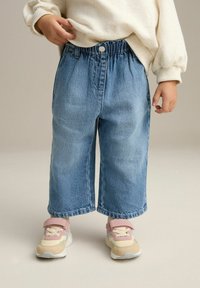 Culottes en denim bleu clair avec une taille élastique, dotés de poches latérales et d'une coupe décontractée. Associés à des baskets pastel.