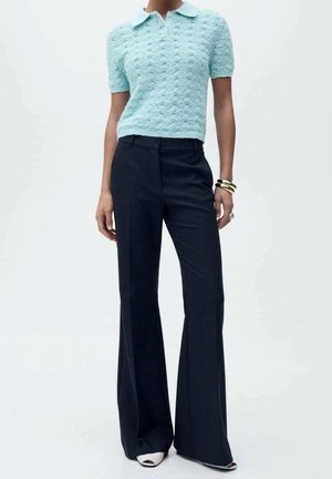 Jasnoniebieska, krótki rękaw, teksturowana dzianinowa koszulka polo w połączeniu z ciemnymi, szerokimi spodniami. Spodnie mają wyprasowane kanty i klasyczny krój.