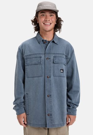 Lichtblauwe denim shirtjack met een voor sluiting met knopen, twee borstzakken en een logopatch. Heeft een ontspannen pasvorm en lange mouwen.