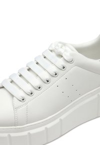 Vit sneaker med en texturerad läderöverdel, platta snören och perforerade detaljer. Tjock, ribbad sula för ökad höjd och stabilitet.