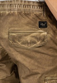 Braune strukturierte Shorts mit einem elastischen Bund, einer Gesäßtasche mit geschwungener Naht und einem schwarzen Etikett mit weißer Schrift.