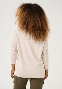 Hellbeiger, gerippter Strickpullover mit langen Ärmeln und lockerem Schnitt, kombiniert mit olivgrünen Cargohosen. Strukturierter Stoff mit weichem Finish.