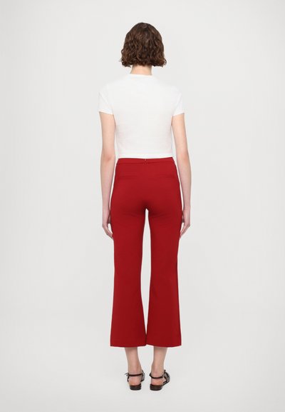 Pantalon large rouge avec une texture lisse, doté d'une taille mi-haute et de poches arrière. Associé à un crop top ajusté blanc.