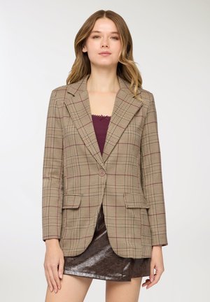 Blazer a quadri marrone con design aderente, chiusura con un solo bottone, due tasche frontali e rever a lancia. Indossato sopra una maglia color borgogna.