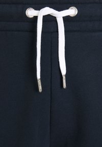 Pantalon de survêtement bleu marine avec un cordon blanc passé à travers des œillets métalliques et des embouts métalliques aux extrémités.