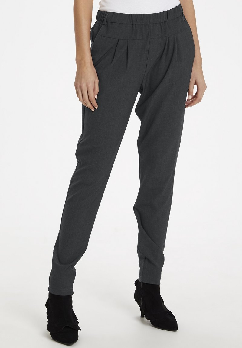 Pantalon gris taille haute avec un devant plissé, fabriqué en tissu doux. Doté de poches latérales et de jambes effilées. Longueur jusqu'au sol.