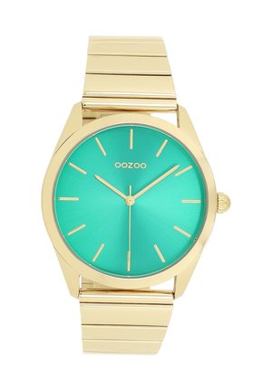 Montre avec un bracelet en métal doré et un cadran rond, présentant un fond teal, des index et aiguilles dorés, avec la marque 'OOZOO' affichée.