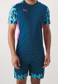 Námořnický set sportovního oblečení obsahující tričko s krátkým rukávem modrými geometrickými vzory a růžovými akcenty, doplněné o odpovídající šortky se stejnými designy.