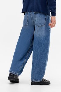 Blue denim wide-leg jeans with a textured finish, five pockets, and a loose fit, paired with black shoes. The fabric is slightly faded.