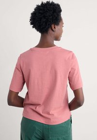 Jasnoróżowy t-shirt z krótkim rękawem i okrągłym dekoltem, wykonany z miękkiej bawełny, o luźnym kroju i bocznych rozcięciach u dołu.