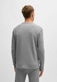 Grijze textuur met lange mouwen, ronde hals en geribde manchetten, gecombineerd met bijpassende broek, die een samenhangende kleur en ontwerp laat zien.