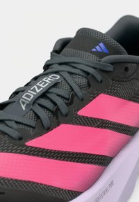 Gros plan sur une chaussure de course Adidas Adizero noire et rose avec des lacets gris et une semelle Lightstrike Pro.