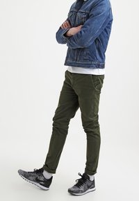 Gröna bomullschinos med slim fit, med en slät textur. Tillsammans med en denimjacka och sneakers i svart och grått mönster.