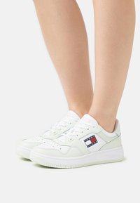 Baskets blanches et vert clair avec un bout perforé, un patch logo sur le côté et une semelle en caoutchouc ; matériaux en cuir lisse et en tissu.