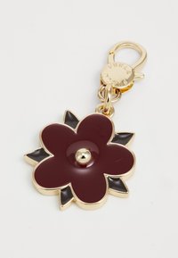 Porte-clés en fleurs dorées et bordeaux avec des accents de feuilles noires et un fermoir doré gravé "Furla" sur un fond blanc.