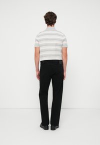 Polo de manga corta a rayas en gris y blanco combinado con pantalones negros de pierna recta. El conjunto presenta un ajuste casual y un detalle minimalista.
