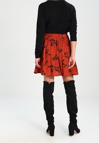 Jupe fleurie rouge à taille froncée, associée à un haut noir à manches longues et des bottes en suède noires montant au-dessus du genou.