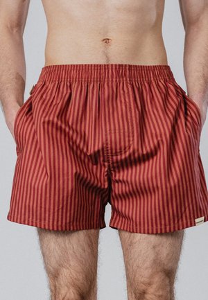 Männlicher Oberkörper und obere Beine, bekleidet mit rot und dunkelrot vertikal gestreiften Boxershorts mit elastischem Bund und seitlichen Taschen.