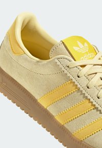 Světlé žluté semišové tenisky s třemi žlutými pruhy, texturovanou podrážkou a žlutým jazykem s logem Adidas.