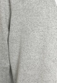 Tejido de punto gris claro con un acabado texturizado, que presenta sutiles variaciones en el color y una apariencia suave y cómoda.