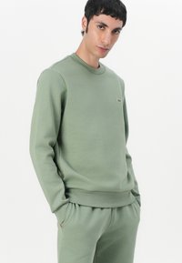 Grüne Sweatshirt aus Baumwollmischung, Rundhals, gerippte Bündchen und Saum; verfügt über ein kleines Logo auf der Brust; glatte Textur. Kombiniert mit passenden Hosen.