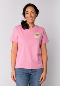 Rosa Baumwoll-T-Shirt mit kurzen Ärmeln, das auf der linken Brustseite eine kleine Herzgrafik in Regenbogenfarben zeigt. Lässiger Schnitt und weiche Textur.