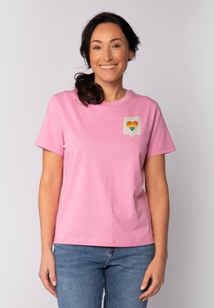 T-shirt en coton rose à manches courtes avec un petit graphique en forme de cœur aux couleurs de l'arc-en-ciel sur la zone gauche de la poitrine. Coupe décontractée et texture douce.