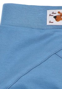 Ljusblått tyg med en ribbad midja; har ett märke med en tecknad hunddesign och texten "How How How." Mjuk textur, avslappnad passform.
